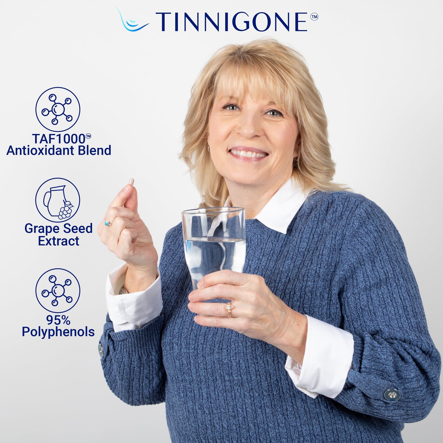 A woman smiling and holding a Tinnigone pill and glass of water